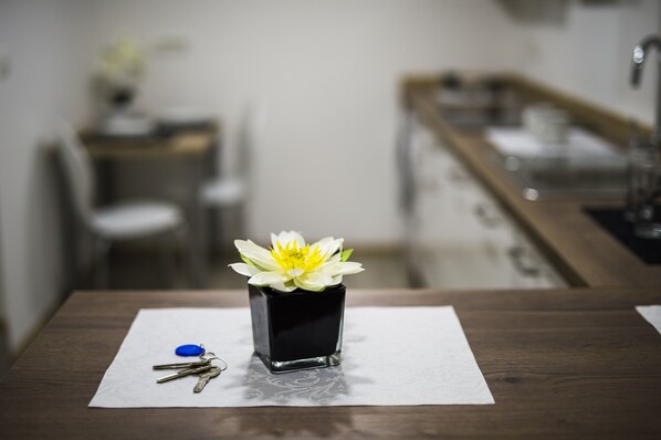 A small black vase with a white flower on a table in a room.