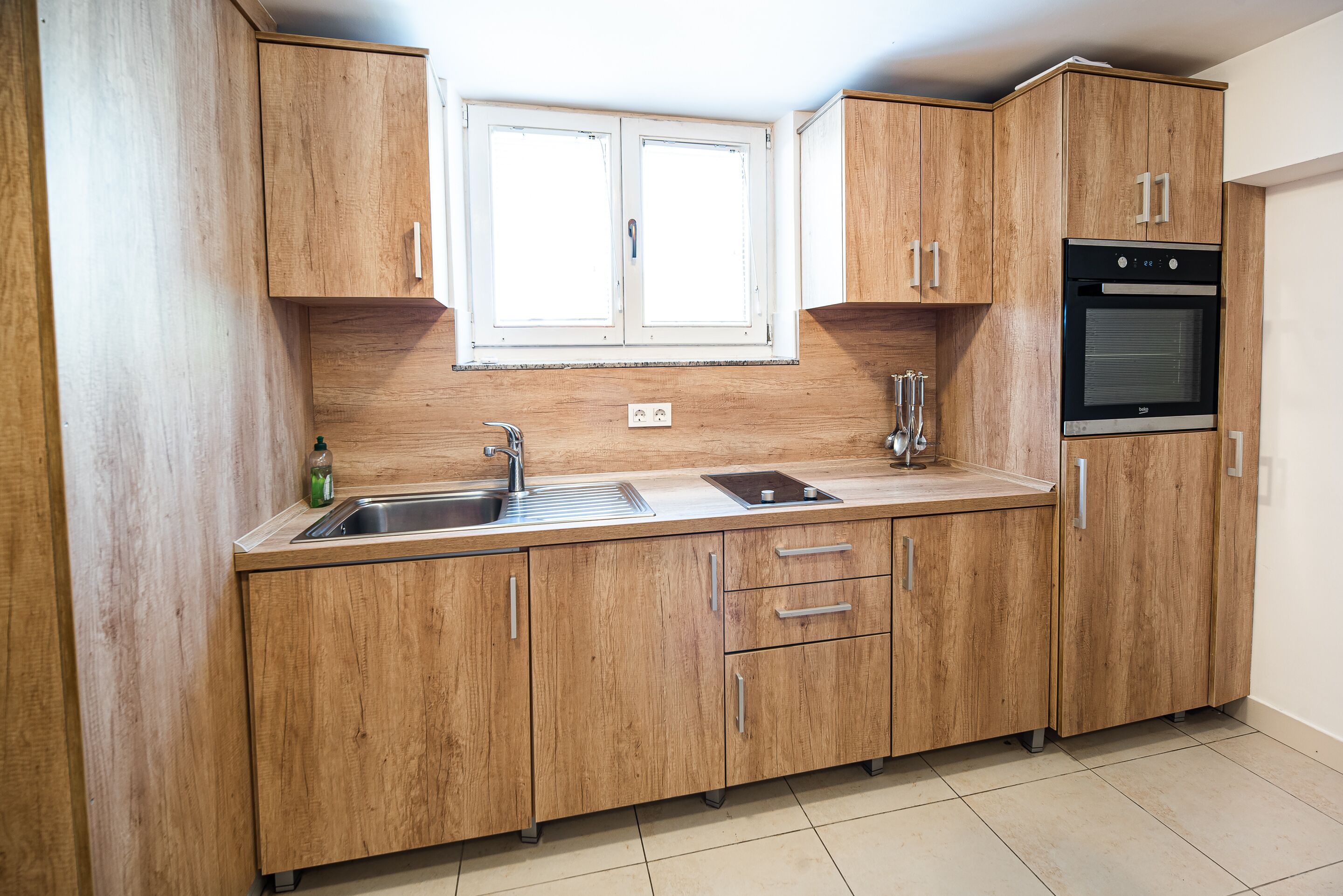Une cuisine avec des meubles de rangement en bois, un évier à deux bacs et un four encastré.