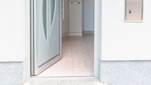 A modern entrance with a glass door, a small step leading up to the door, and a light switch on the wall. - Studio Enig (Izola)
