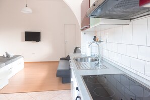 A modern kitchen with a built-in stove, a sink, and a flat-screen TV mounted on the wall.
