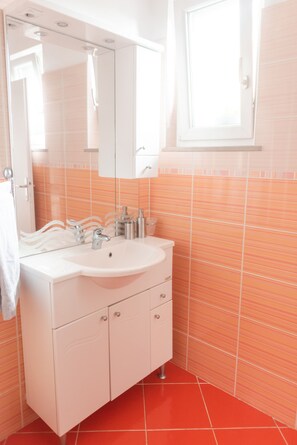 Un bagno con un mobile lavabo bianco, uno specchio grande e pareti piastrellate color arancio.