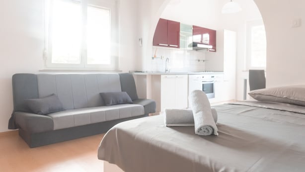 A modern bedroom with a bed, a sofa, and a kitchen in the background. - Studio Enig (Izola)