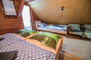 A cozy attic bedroom with two bunk beds, a wooden sloped ceiling, and a window with a lace curtain.