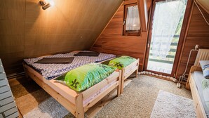 Ein Schlafzimmer im Mansardenstil mit schrägen Wänden, einem Einzelbett mit gemusterten Textilien, einem kleinen Fenster mit Spitzenvorhängen und einem Heizkörper in der Nähe der Tür.