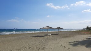 Ein Strand mit zwei Reetsonnenhütten und einem Sandufer.