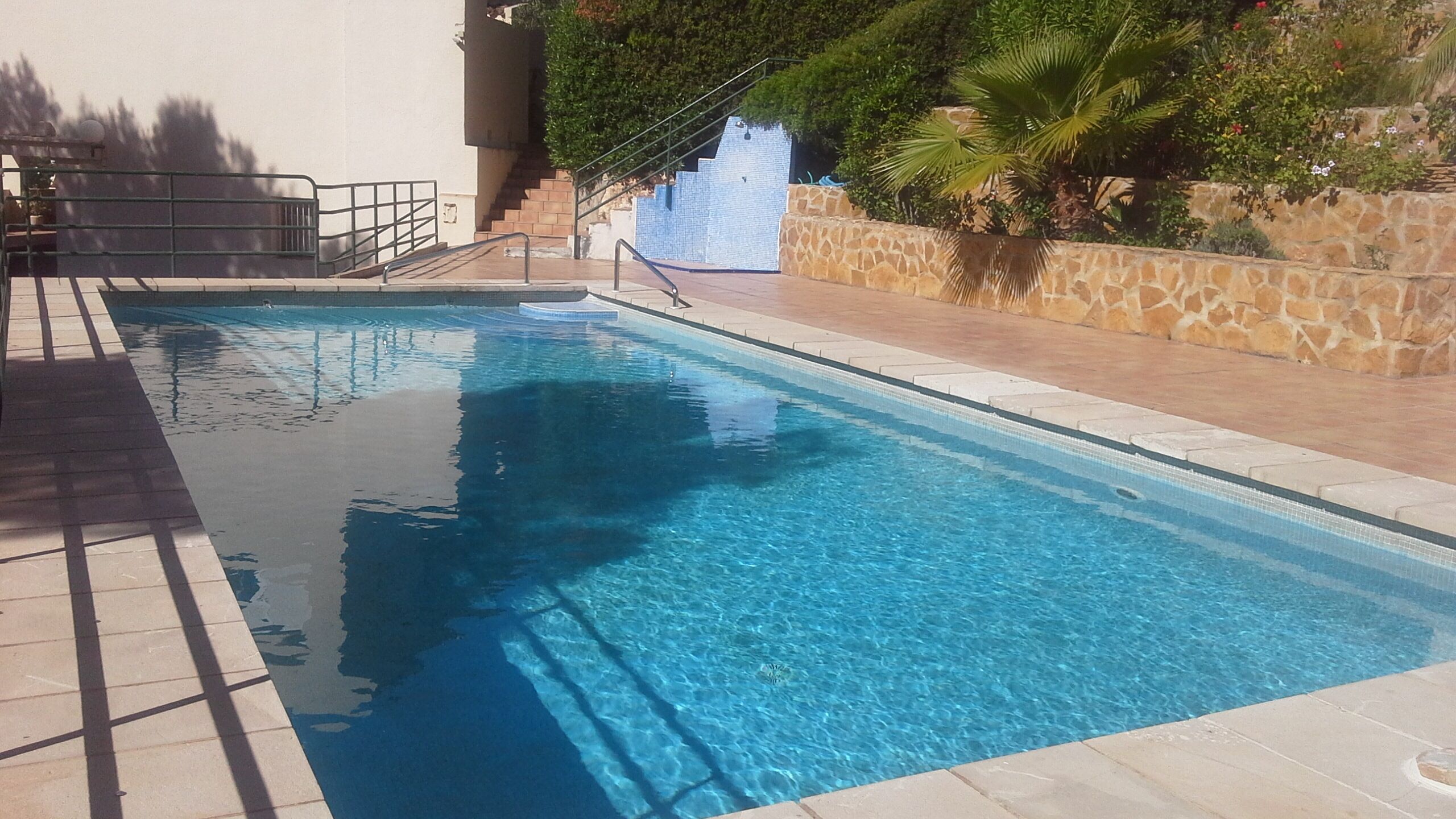 A clear swimming pool with a stone wall and steps leading down to it.