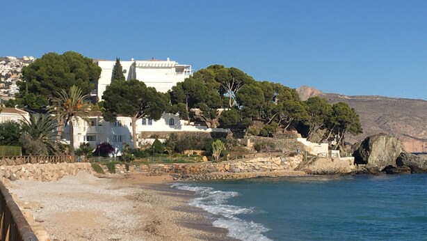 A coastal building with a rocky shoreline, surrounded by trees and a clear blue sky. - Spacious duplex, beautiful view of the golf course and sea. 120 m2. 5 mn from the beach  (Altea)