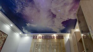 Une pièce avec un plafond décoré d’un ciel étoilé, une fenêtre avec des rideaux et un meuble en bois.