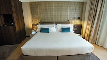 Een groot bed met een gestreept hoofdbord, twee nachtkastjes met lampen en een houten garderobe.
