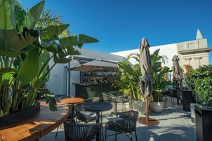 Un espace extérieur aménagé en terrasse, avec des tables et des chaises rondes, entouré de grands pots de plantes et de parasols.