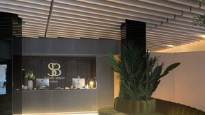 A reception desk with a logo, a computer, a vase with flowers, and a potted plant. - SOHO BOUTIQUE CATEDRAL (Seville)
