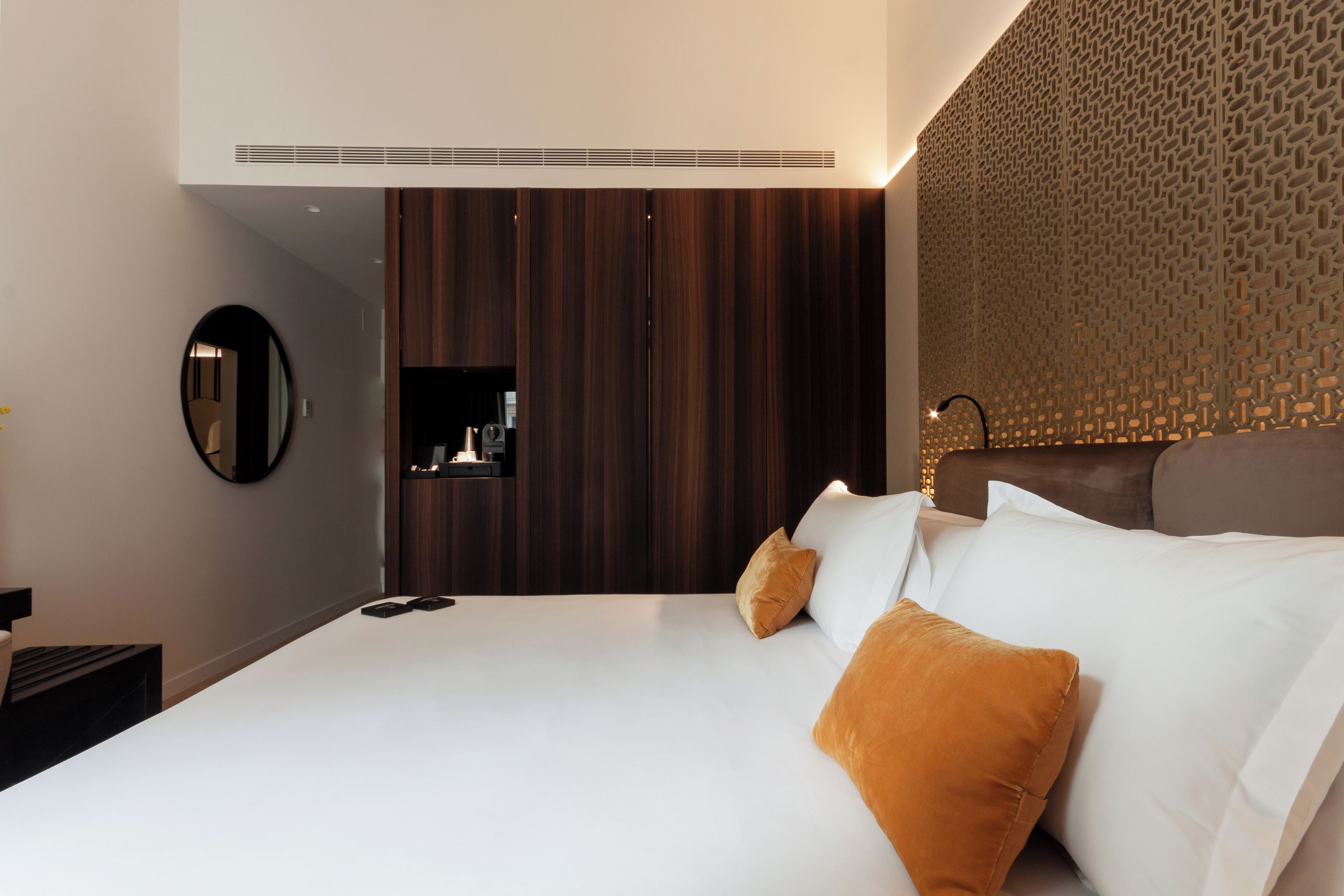 Een moderne hotelkamer met een groot bed, een donker houten garderobe, een ronde spiegel en een behang met een patroon.