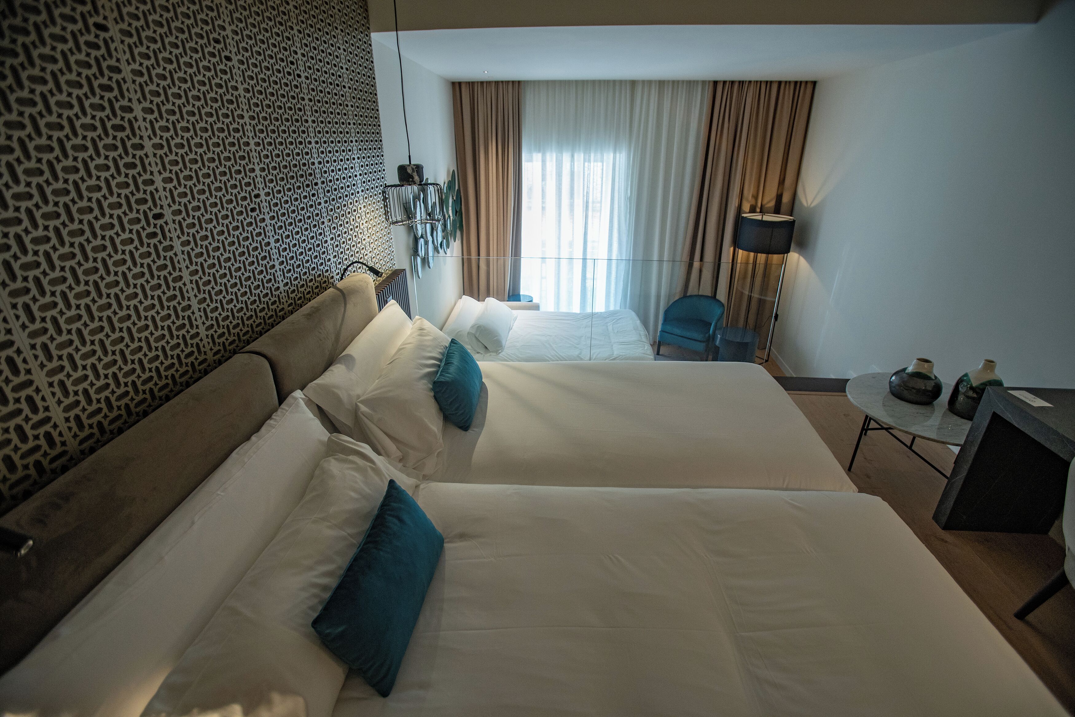 Una habitación de hotel con dos camas, una mesita, una silla y una lámpara.
