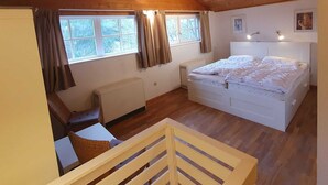 Ein Schlafzimmer mit schrägen Wänden, einem Bett, einem Fenster und einer Heizung.