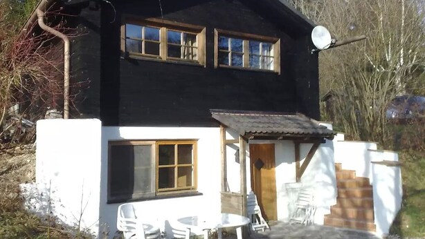 Ein zweistöckiges Haus mit Satellitenschüssel, einer kleinen Veranda mit Stühlen und einer Steinterrasse.