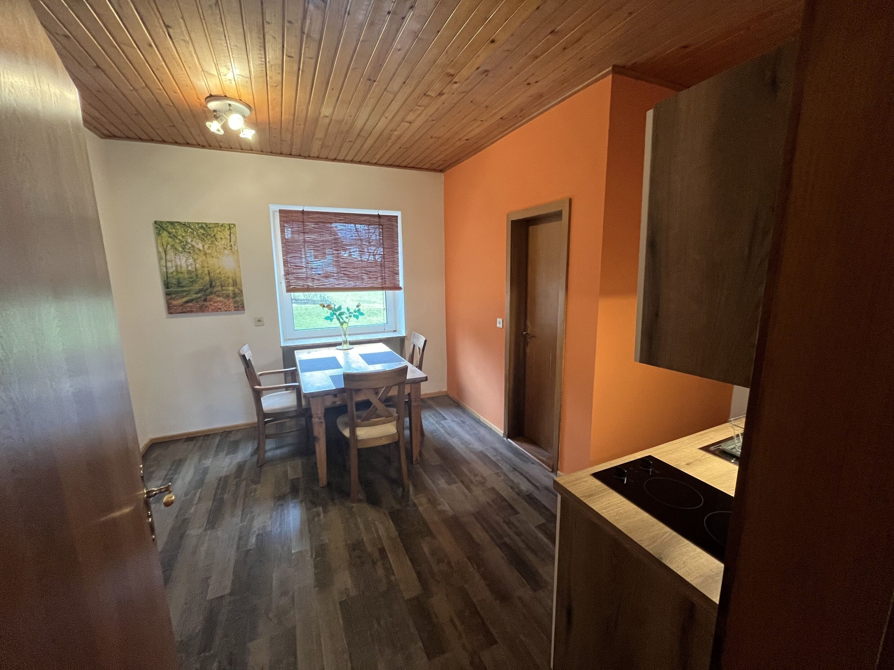Una habitación con mesa, sillas, ventana con vistas, puerta y zona de cocina con estufa.