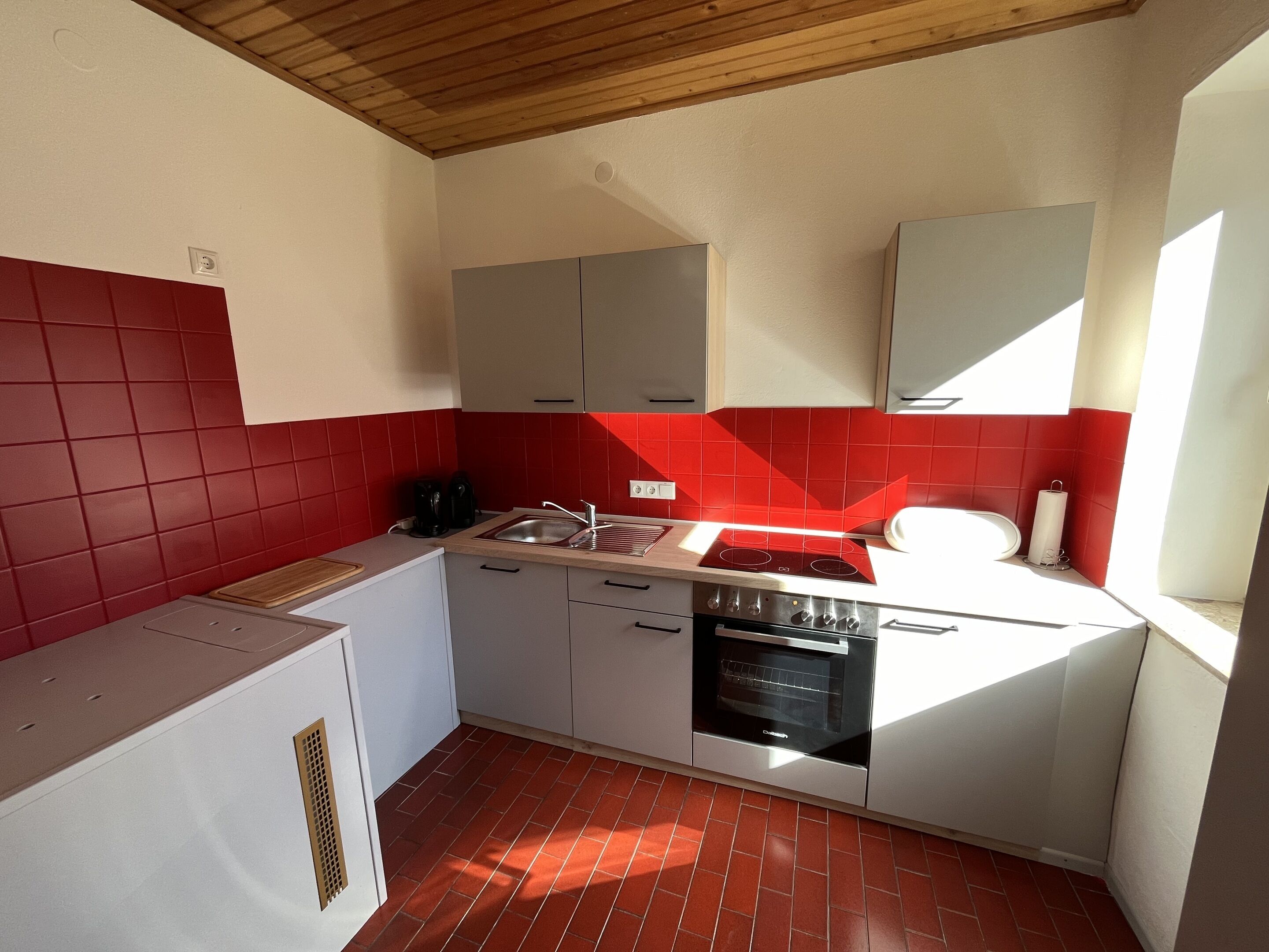 Cocina compacta con salpicadero de azulejos rojos, horno empotrado y un lavabo.