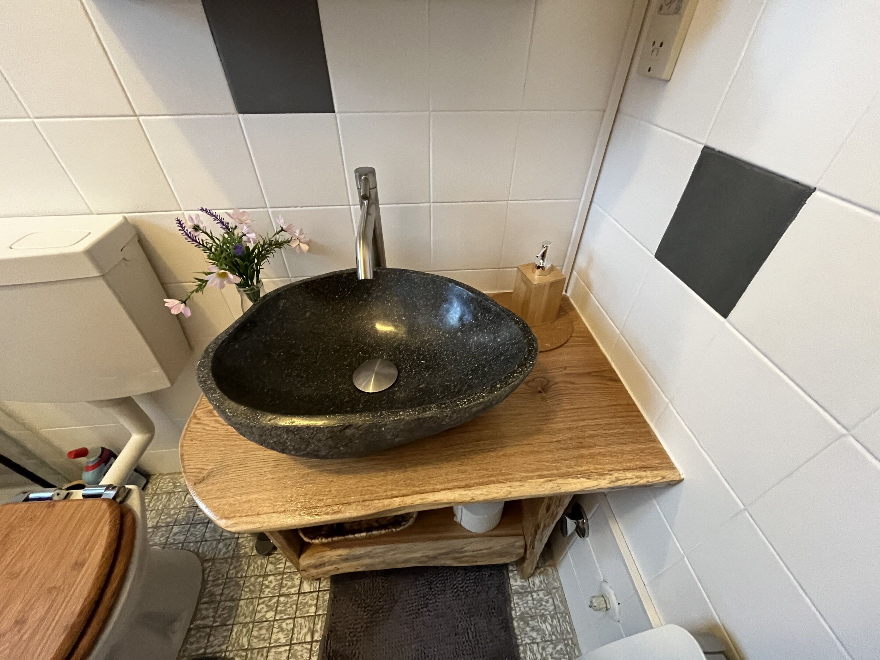 A bathroom with a black stone sink, wooden countertop, and white tiled walls.