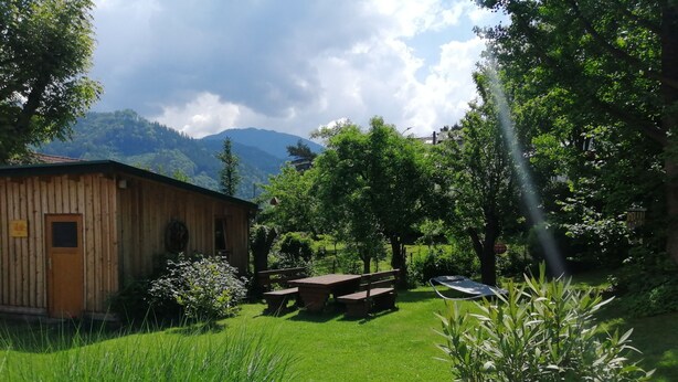 Une cabane en bois avec une table de pique-nique et des bancs, entourée d’une végétation luxuriante et dominant un paysage montagneux.