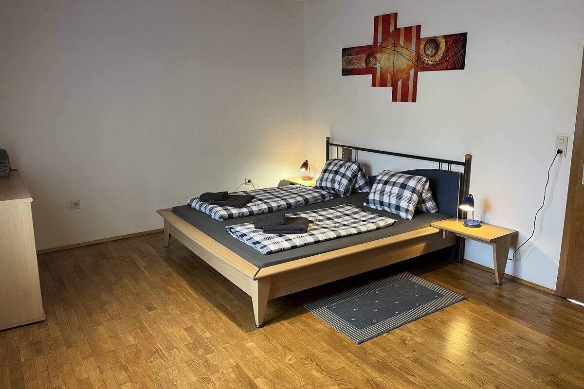 Une chambre avec un lit en bois, une table de chevet avec une lampe, une œuvre d’art murale et un plancher en bois.
