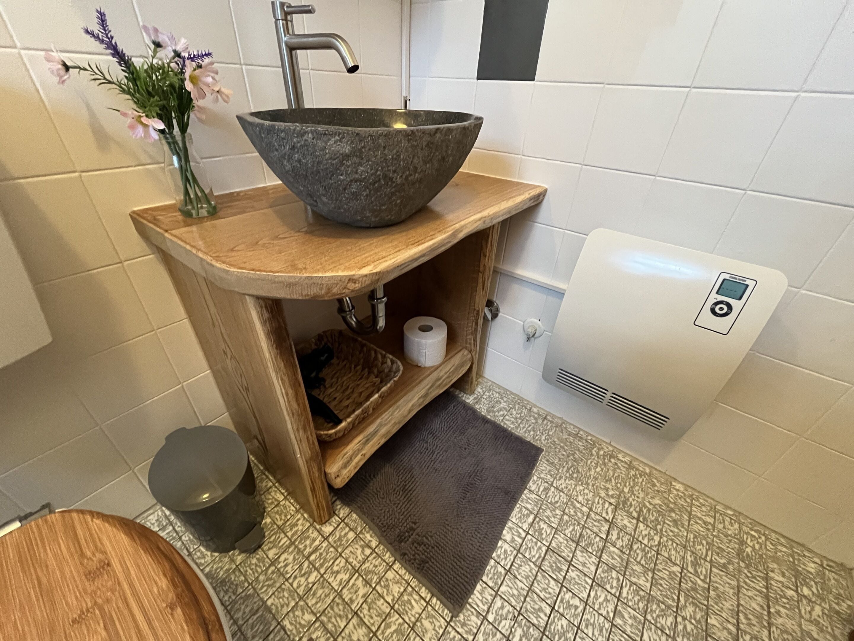 Ett badrum med ett handfat i sten, en trähylla, toalettpapper och en handtork.