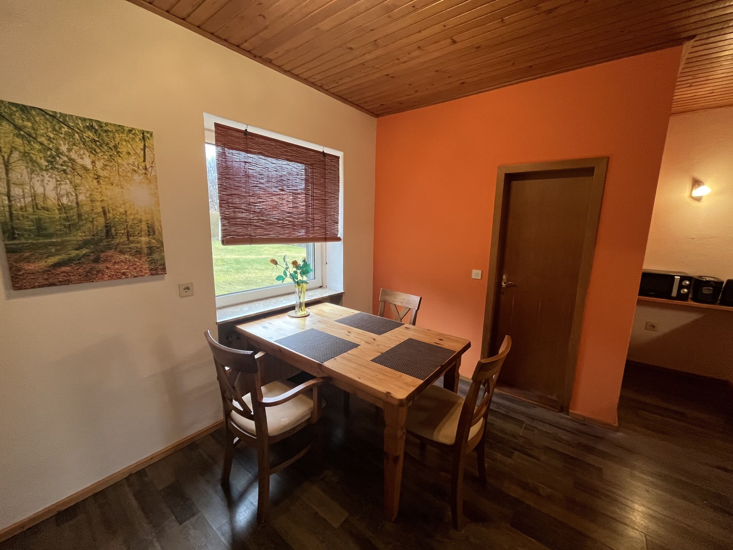 A dining area with a wooden table, chairs, a window with blinds, and a painting on the wall.