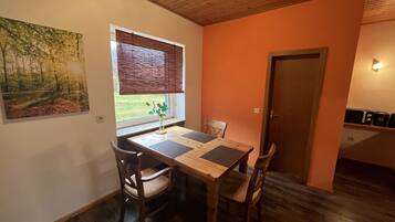 A dining area with a wooden table, chairs, a window with blinds, and a painting on the wall.