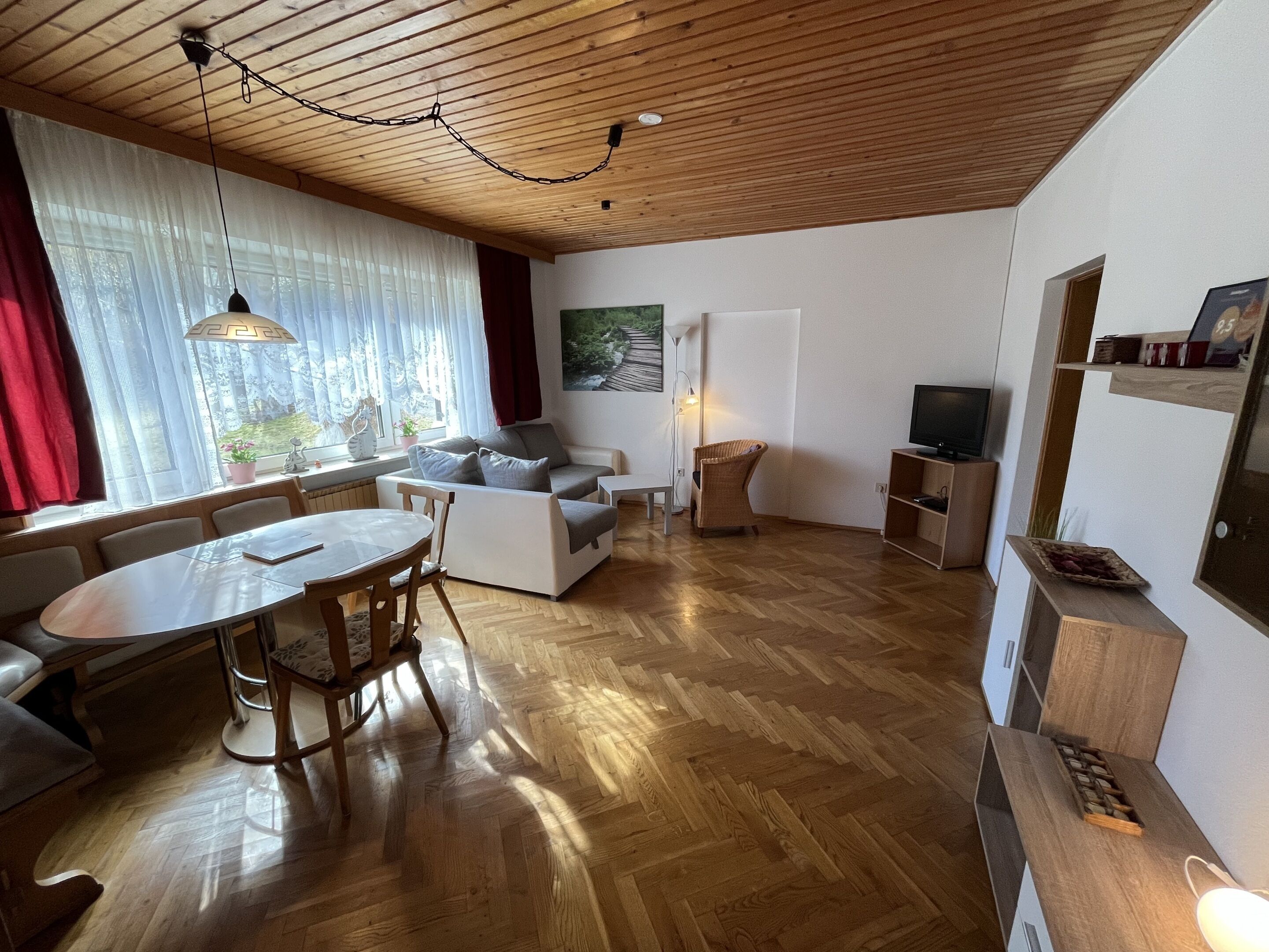 A modern living room with a sofa, dining table, and chairs, wooden flooring, and a television.