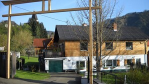 Une maison en bois avec un garage vert, une allée couverte et une vue sur les montagnes en arrière-plan.