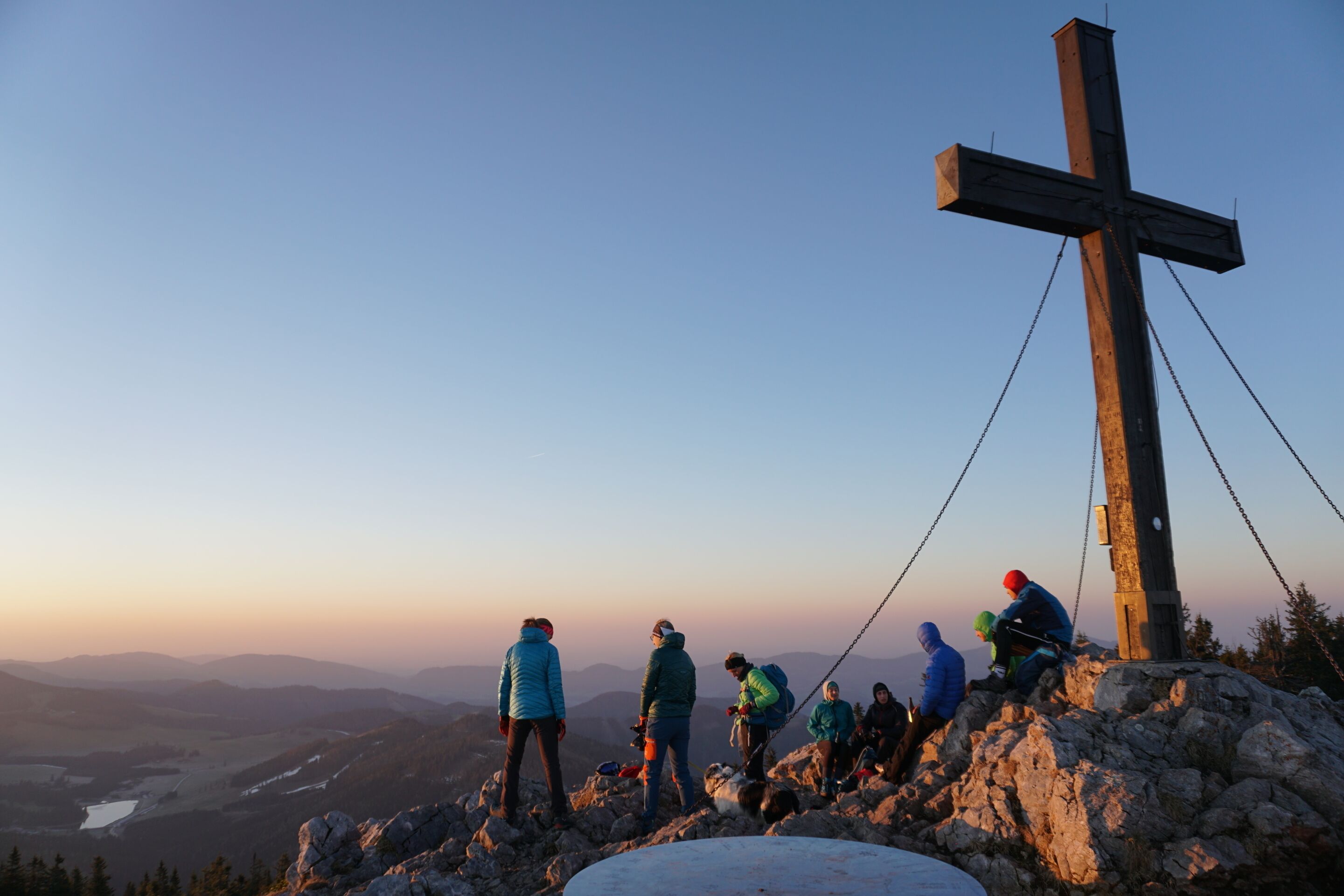 A group of hikers on a mountain with a wooden cross in the background.