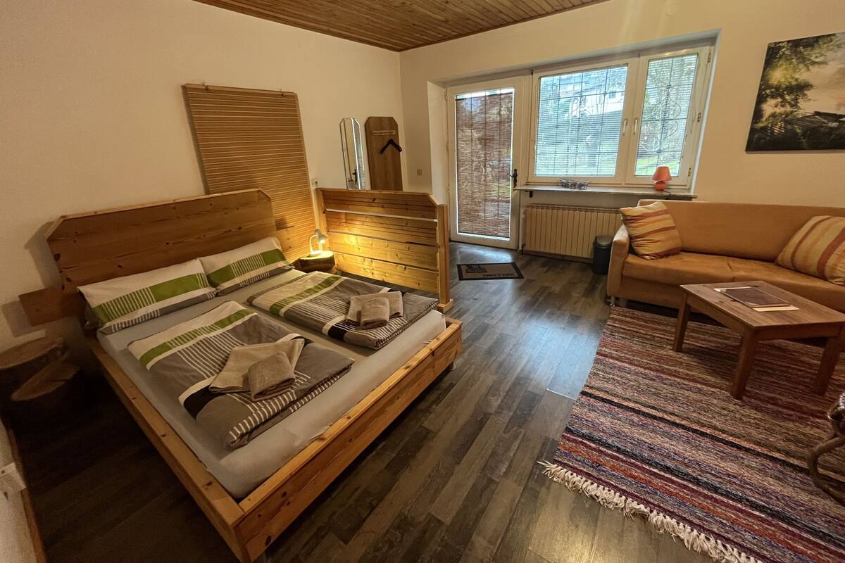 Une pièce confortable avec un lit en bois, un canapé et une fenêtre équipée de stores.