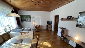 Un salon moderne avec un plancher en bois, une table à manger, un canapé, un téléviseur et un tableau accroché au mur.