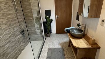 Un baño moderno con cabina de ducha de vidrio, tocador de madera con un lavamanos grande y un espejo sobre el tocador.