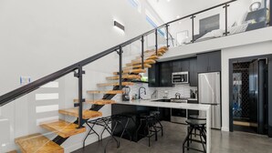 Een moderne keuken met een centraal eiland, zwarte barkrukken en een trap met houten treden.