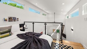 Een moderne slaapkamer met een bed, een glazen scheiding, een plafondventilator en uitzicht op groen buiten.