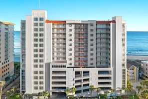 Um hotel moderno com várias varandas, uma garagem de estacionamento e vista para o oceano.