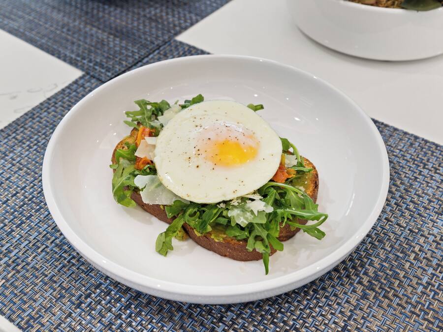 Un plato blanco con pan tostado, vegetales verdes y un huevo frito.