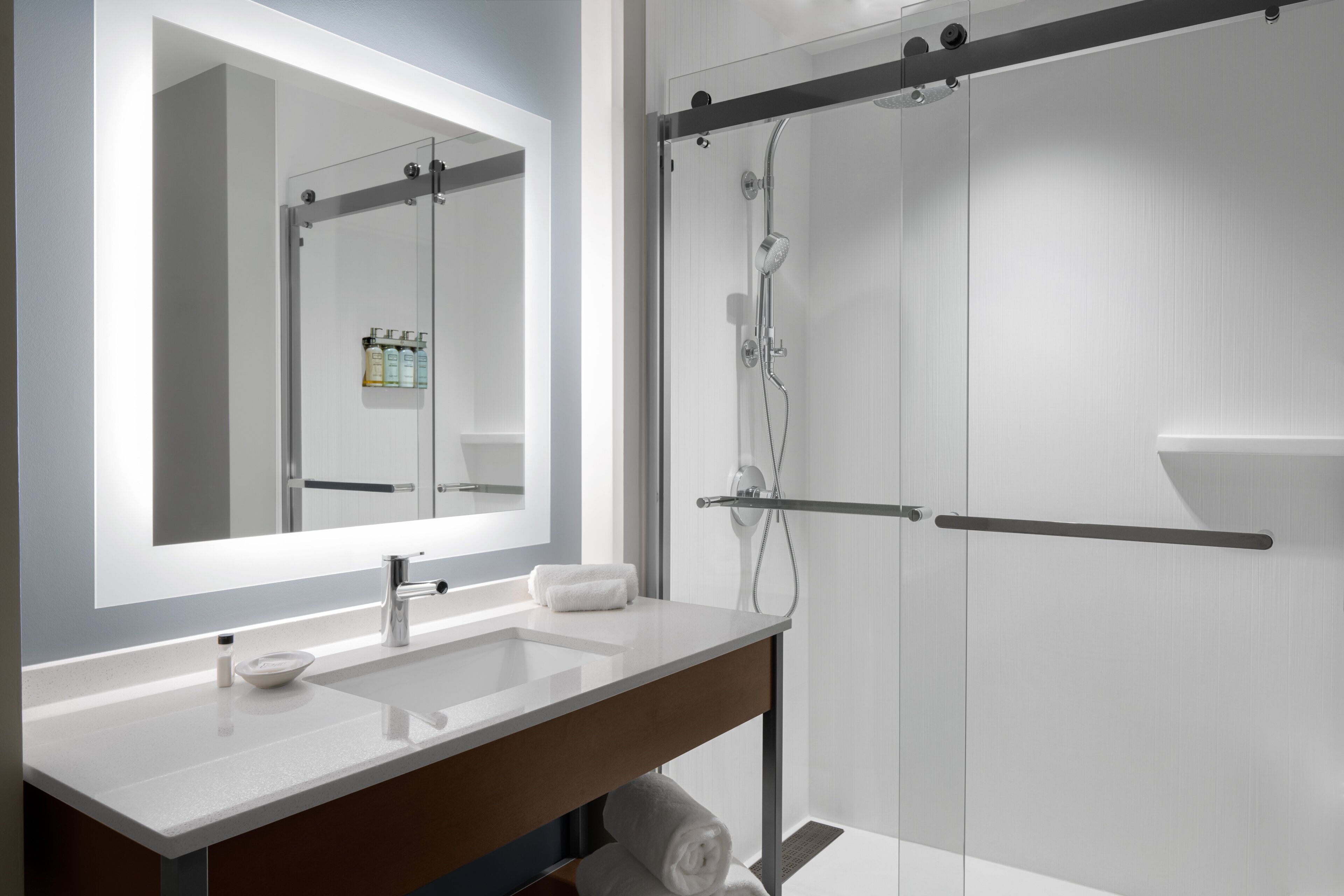 Un baño moderno con un espejo grande, dos lavamanos, una ducha y un perchero para toallas.