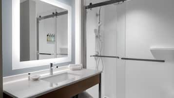 Un baño moderno con un espejo grande, dos lavamanos, una ducha y un perchero para toallas.