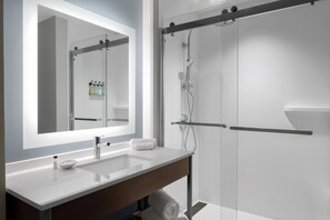 Un baño moderno con un espejo grande, dos lavamanos y una zona de ducha con mampara de vidrio.