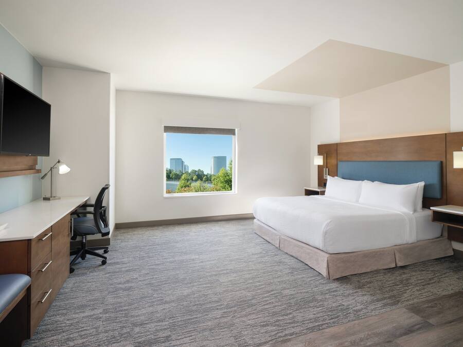 A hotel room with a bed, desk, chair, and a TV mounted on the wall.