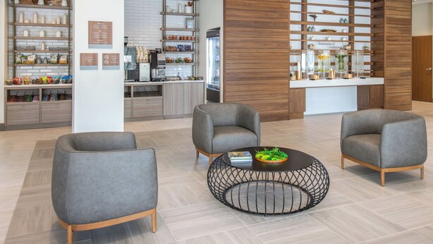 Un vestíbulo moderno con sillones grises, una mesa de centro y una zona de cocina con estantes y electrodomésticos.