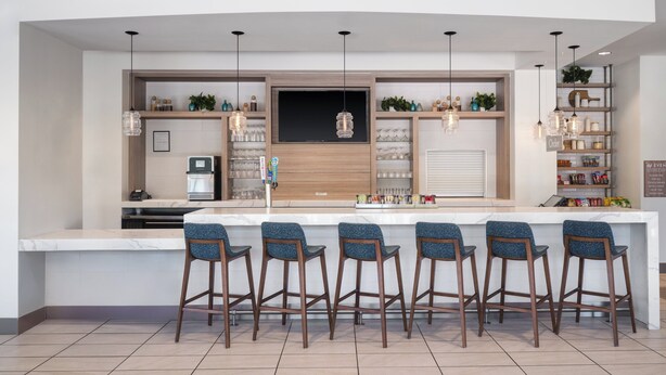 Une cuisine moderne dotée d’un îlot central, de tabourets de bar, de luminaires suspendus et d’étagères intégrées.