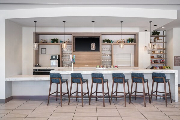 Cocina moderna con una isla central, taburetes de bar, iluminación colgante y estanterías empotradas.