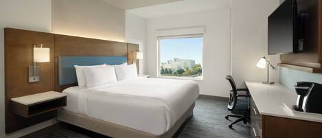 A hotel room with a large bed, a desk, a chair, a TV, and a window with a city view.