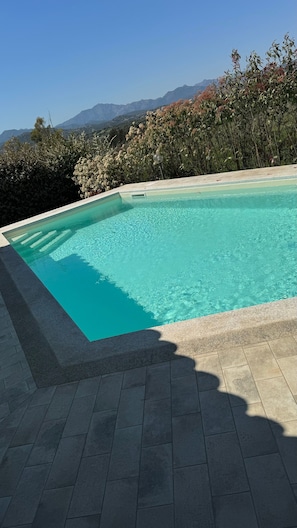 A swimming pool with clear water, surrounded by a tiled deck and a view of mountains in the background. - Idyllic Holiday Home "Oasis of Relaxation" with Garden and Terrace (Budoni)