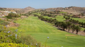 A golf course with a clear view of the green, palm trees, and distant buildings. - Las Terrazas Villa 3 with Sea View, Wi-Fi, Pool, Garden & Terraces (El Salobre)