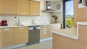 A modern kitchen with wooden cabinets, a dishwasher, a sink, and a window with a view of greenery. - Las Terrazas Villa 3 with Sea View, Wi-Fi, Pool, Garden & Terraces (El Salobre)