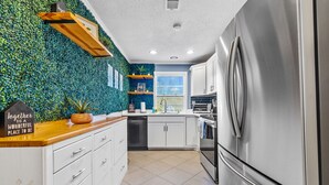 A modern kitchen with white cabinets, a stainless steel refrigerator, and a green wall with plants. - Energy Villa 1-Sleeps 4 (Atlanta)