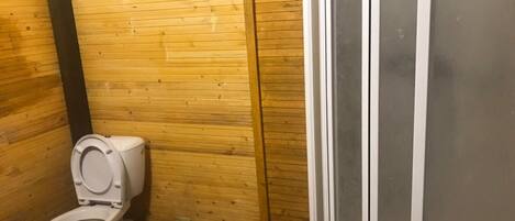 Un baño pequeño con paneles de madera, un inodoro y una zona de ducha.